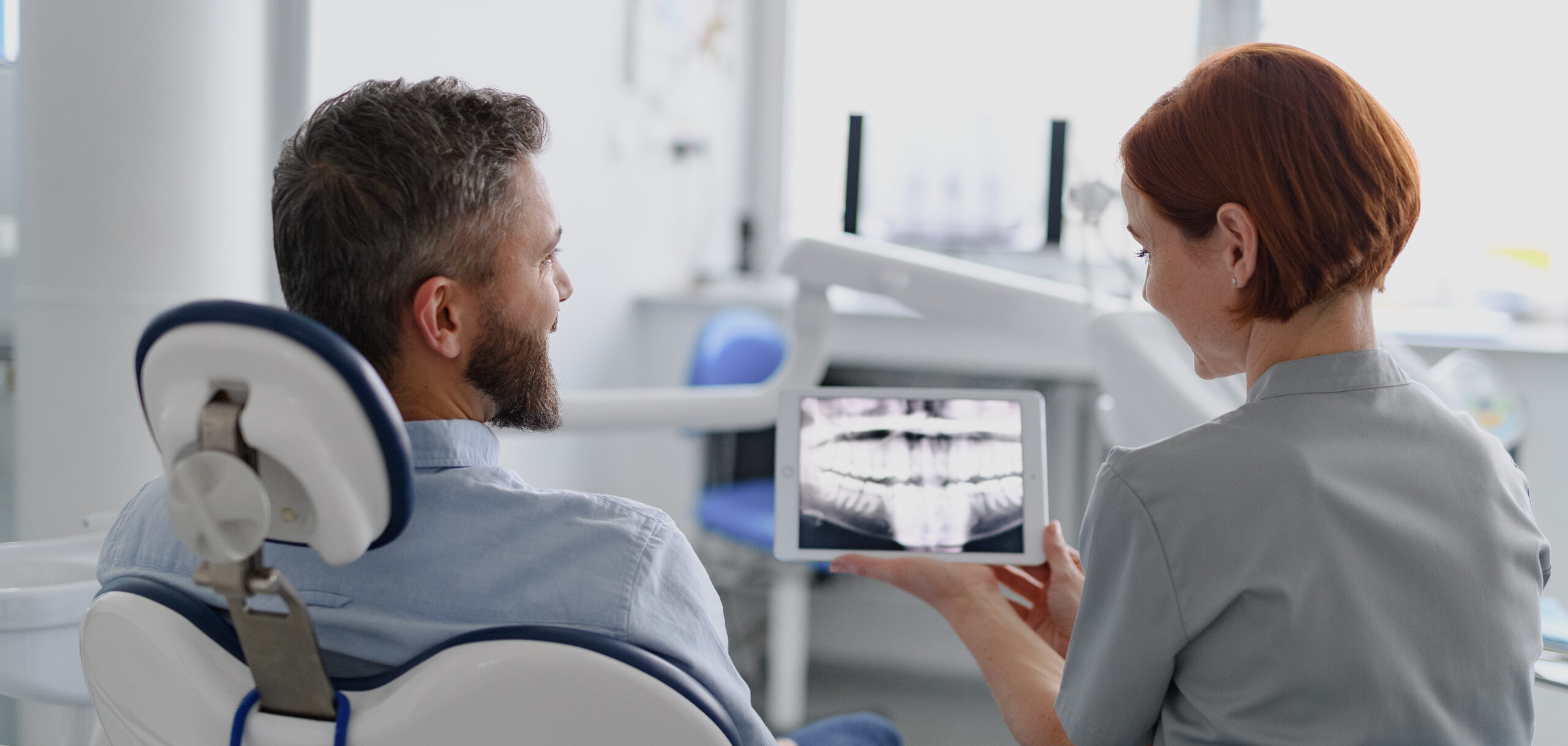 Friendly female dentist showing x-ray to patient in dental clinic during anual check-up. Banner with copy space.
